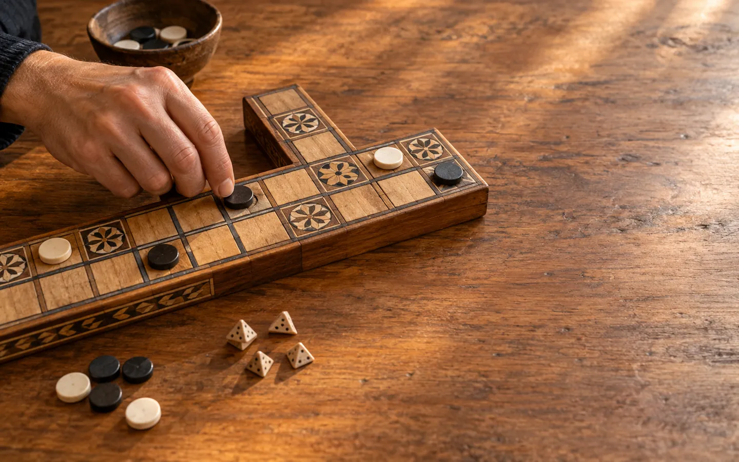 Hands moving a counter on a replica twenty-square race game board with rosette squares, on a wooden table